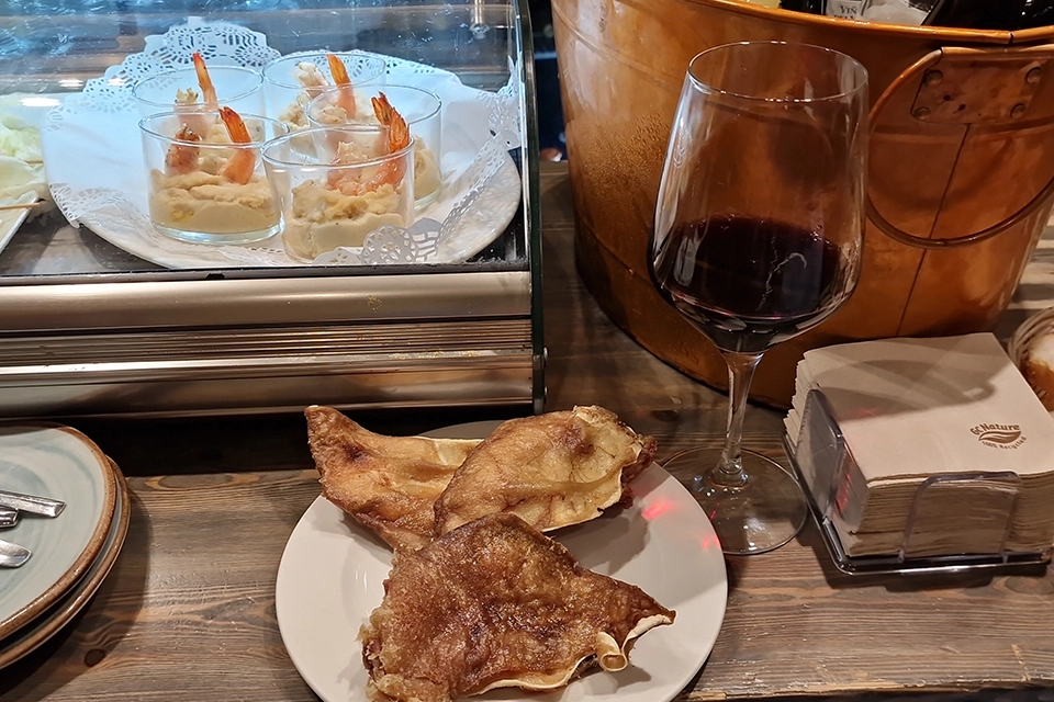 Plato de oreja, copa de vino y cóctel de gambas